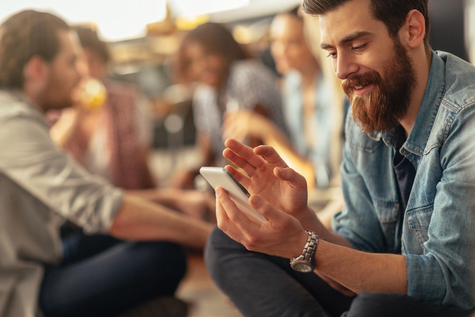 Hombre reunido con amigos y viendo las notificaciones de su App BBVA