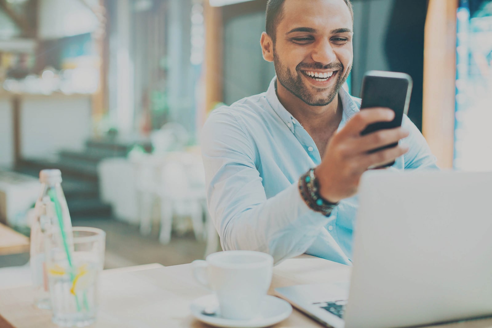 hombre sonríe y usa su celular en cafetería